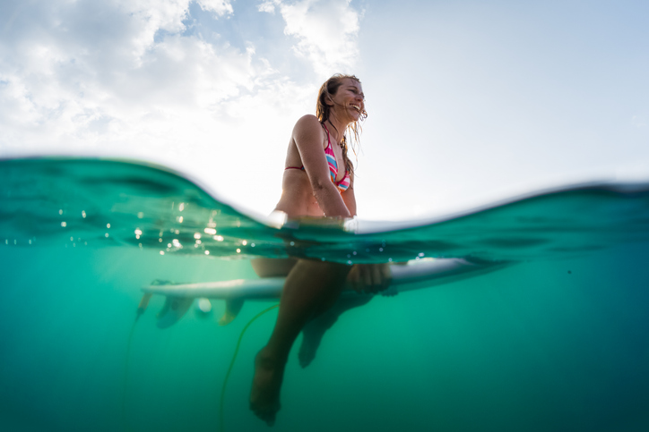 Underwater view of the happy woman sitting on the surfboard